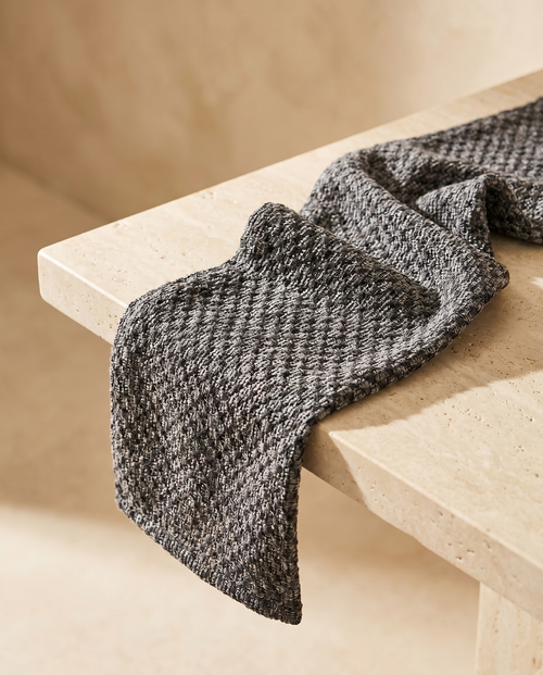 KESA exfoliating shower towel in black, draped on a warm stone ledge