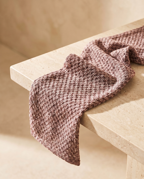 KESA exfoliating shower towel in pink, draped on a warm stone ledge